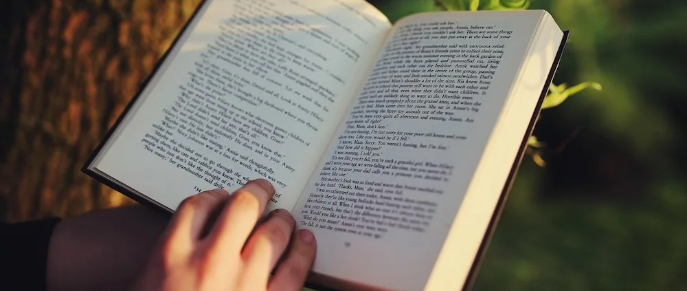 Zeigt ein aufgeschlagenes Buch mit einer Hand am unteren Ende